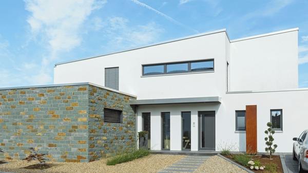 Modernes Einfamilienhaus mit Flachdach, weißer Fassade und Natursteinmauer im Vorgarten.